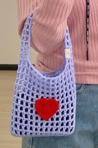 a woman is holding a crocheted bag with a heart on the front and side