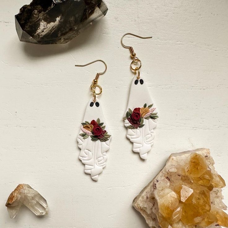 two pairs of earrings with flowers on them next to some rocks and crystal crystals,