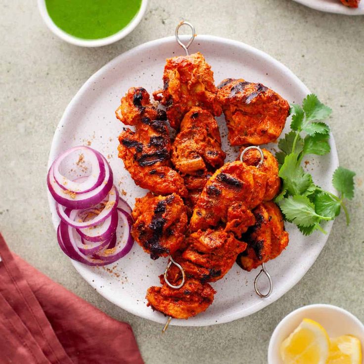 chicken skewers on a plate with onions, cilantro and green tea