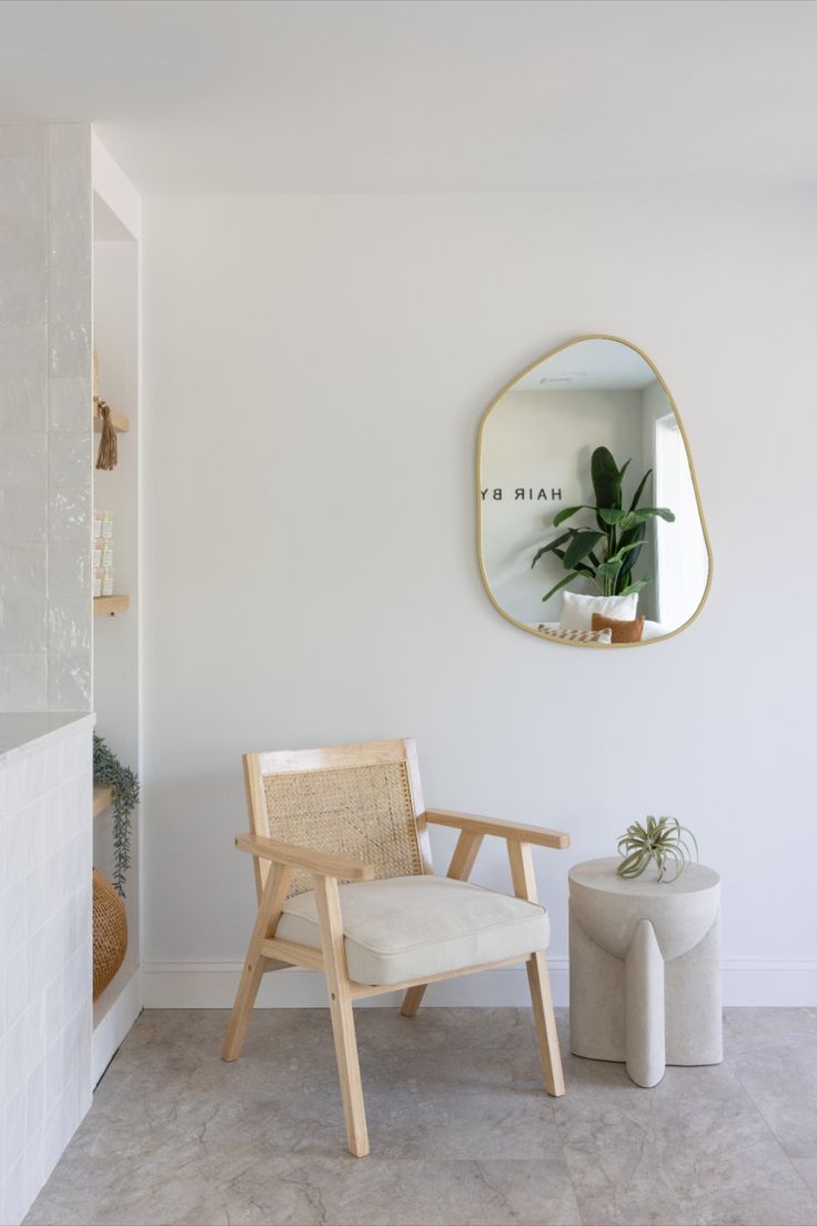 a wooden chair sitting in front of a white wall with a mirror on the wall