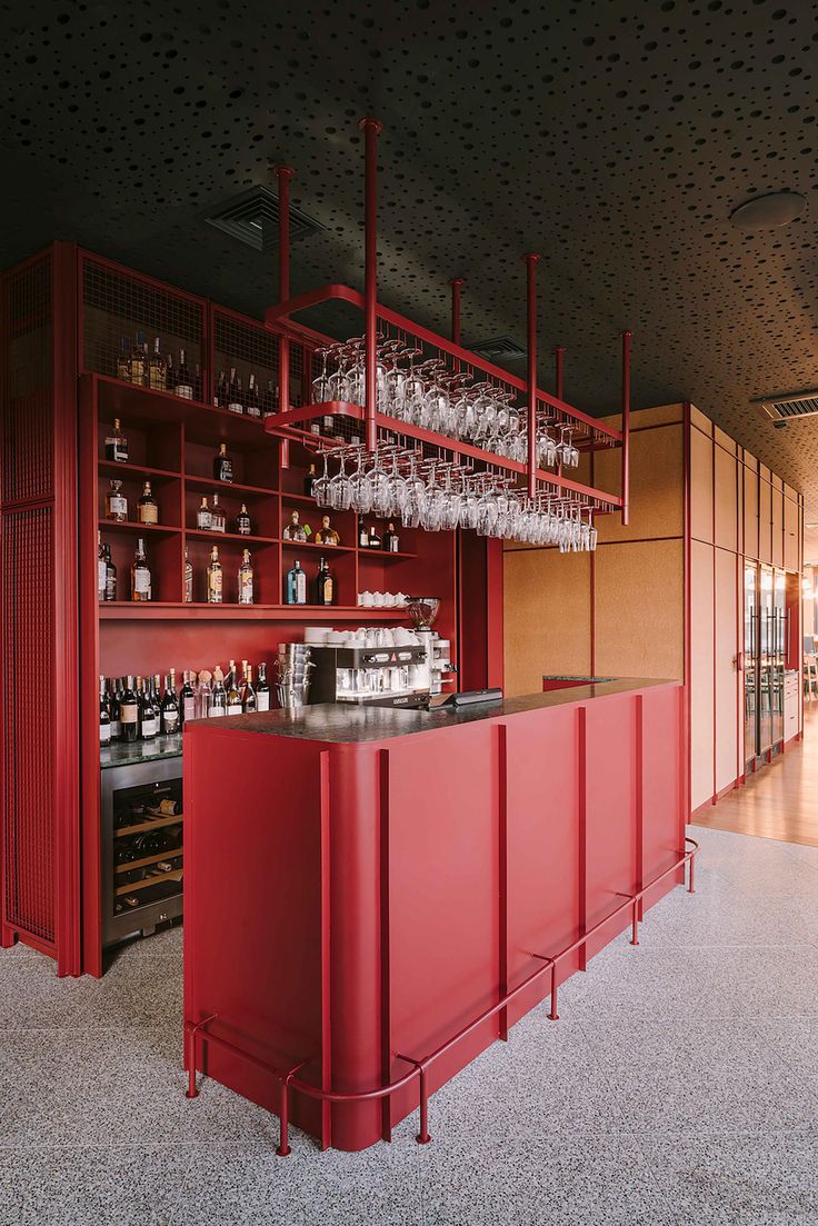 a red bar with lots of wine glasses on the shelves and behind it is a wall full of bottles