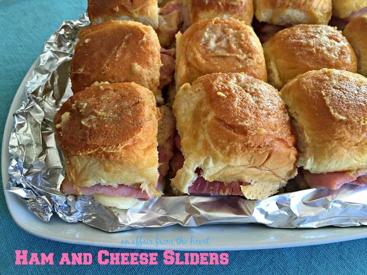 ham and cheese sliders on tin foil lined up on a blue tablecloth with the words ham and cheese sliders