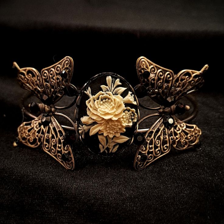 Adjustable Antique Brass Design: Enjoy a perfect fit with the bracelet's adjustable antique brass, blending elegance with comfort for any wrist size. Filigree Butterflies: This bracelet is adorned with delicate brass filigree butterflies, adding a whimsical and enchanting touch to any outfit. Rose Cameo Centerpiece: The 3D Cream-colored rose against a black background offers a timeless appeal to your jewelry collection. Swarovski Crystals: Genuine jet black Swarovski®️ crystals add sparkling bri Adjustable Butterfly Gold Jewelry, Adjustable Gold Butterfly Jewelry, Adjustable Bracelet With Antique Finish, Unique Adjustable Bracelet With Antique Finish, Unique Adjustable Bracelets With Antique Finish, Adjustable Bohemian Bracelet With Antique Finish, Adjustable Filigree Bohemian Cuff Bracelet, Adjustable Filigree Bangle Bracelet, Adjustable Elegant Bronze Cuff Bracelet