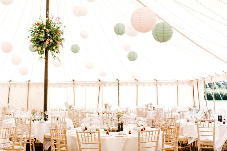 the inside of a tent with tables and chairs set up for a wedding reception under paper lanterns