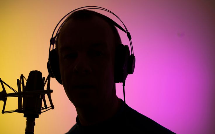 a man with headphones and a microphone in front of a colored background is silhouetted