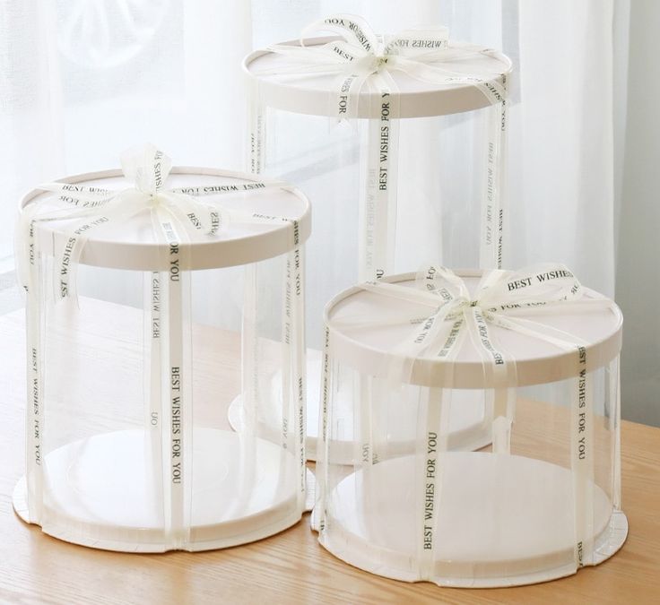 three clear plastic containers with ribbons on them sitting on a wooden table in front of a window