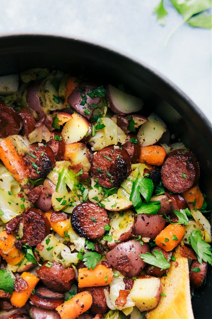 a skillet filled with potatoes, carrots and other veggies next to a wooden spoon