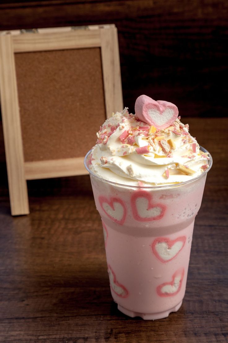 a pink drink with white frosting and hearts on the rim next to a framed photo