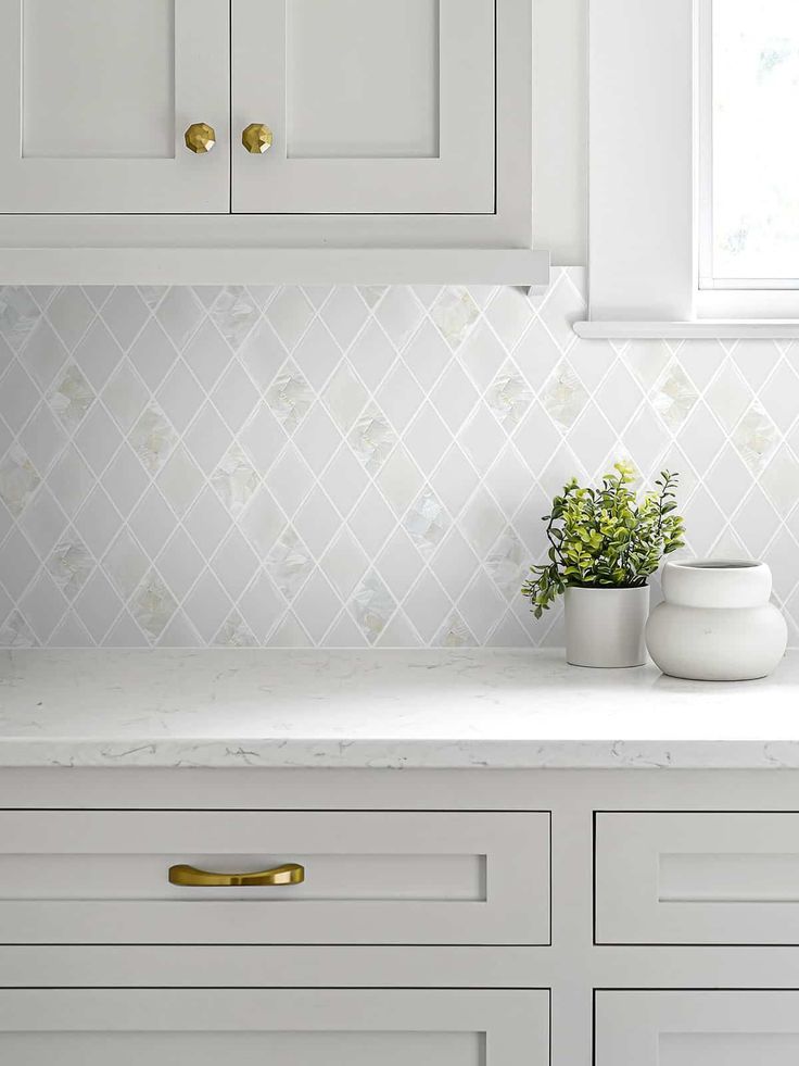 a kitchen with white cabinets and gold pulls on the cupboards next to a potted plant