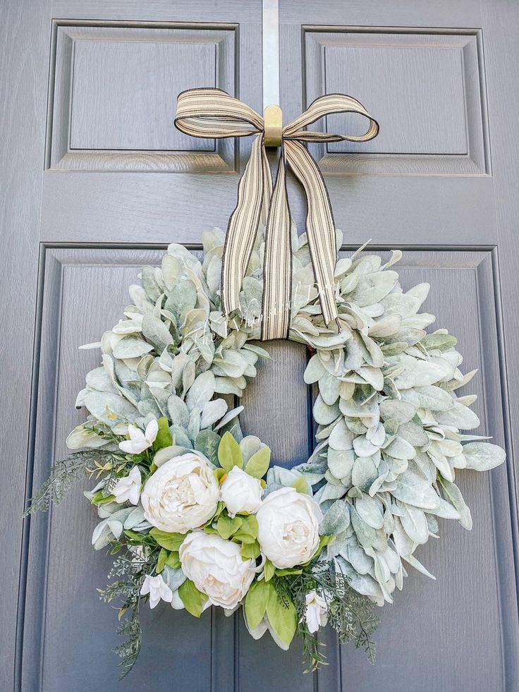 a wreath with white flowers and greenery hangs on the front door of a house