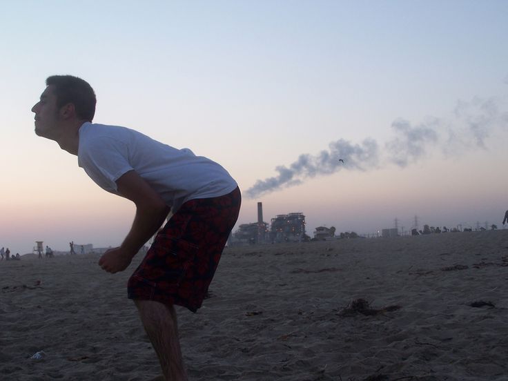 a man standing on top of a sandy beach next to a sky filled with clouds