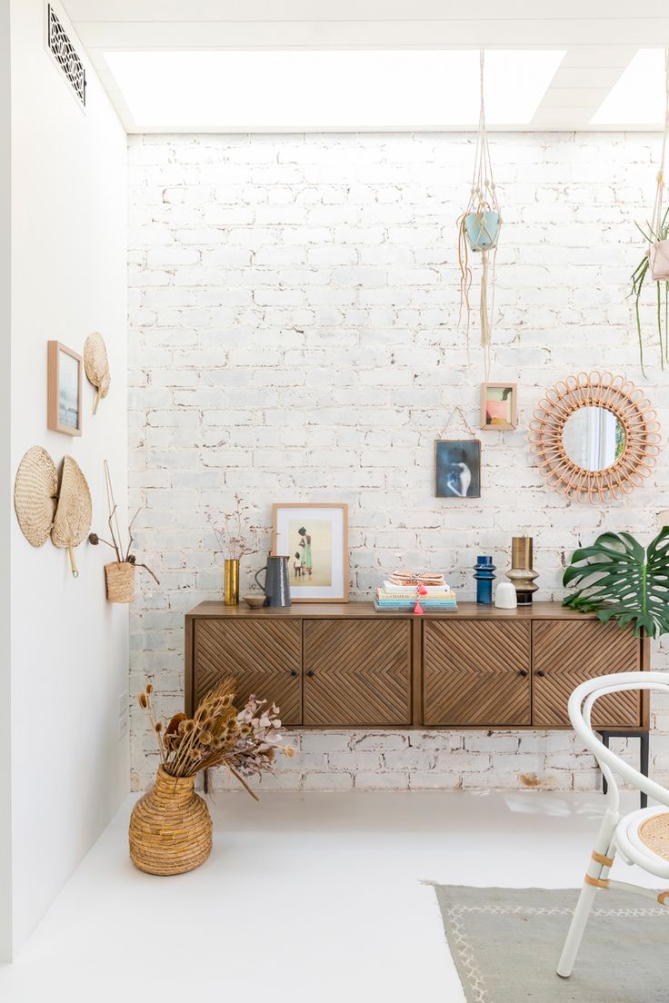 a white brick wall with pictures on it and a wooden dresser in the corner, next to a wicker basket