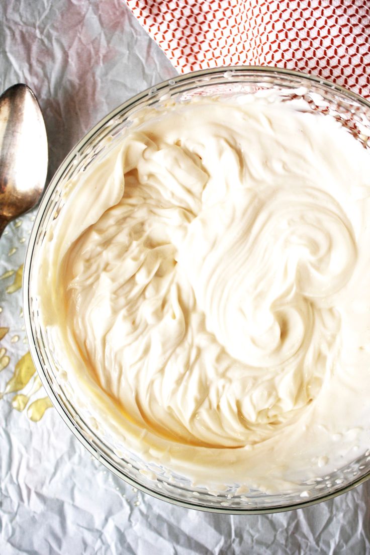 a glass bowl filled with whipped cream next to a spoon on top of a red and white checkered table cloth