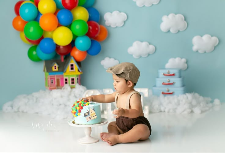 a baby boy sitting on the floor with a cake in front of him and balloons behind him