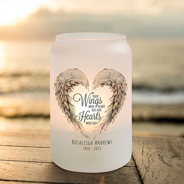 a candle that has been placed on a wooden table near the ocean with an angel wings design