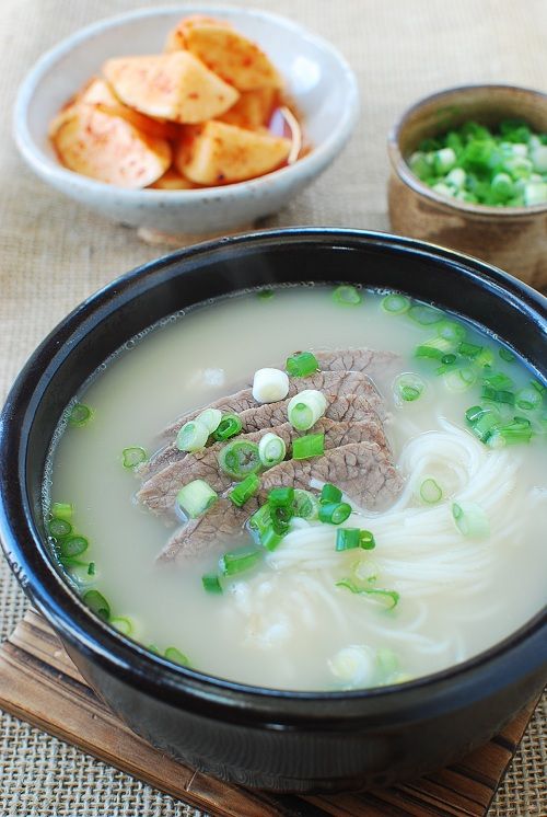 a bowl of soup with meat and green onions in it on a table next to other bowls