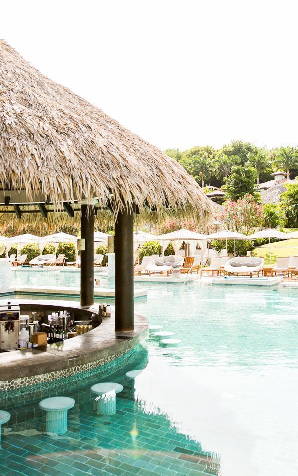 an outdoor bar next to a pool with thatched umbrellas and chairs around it