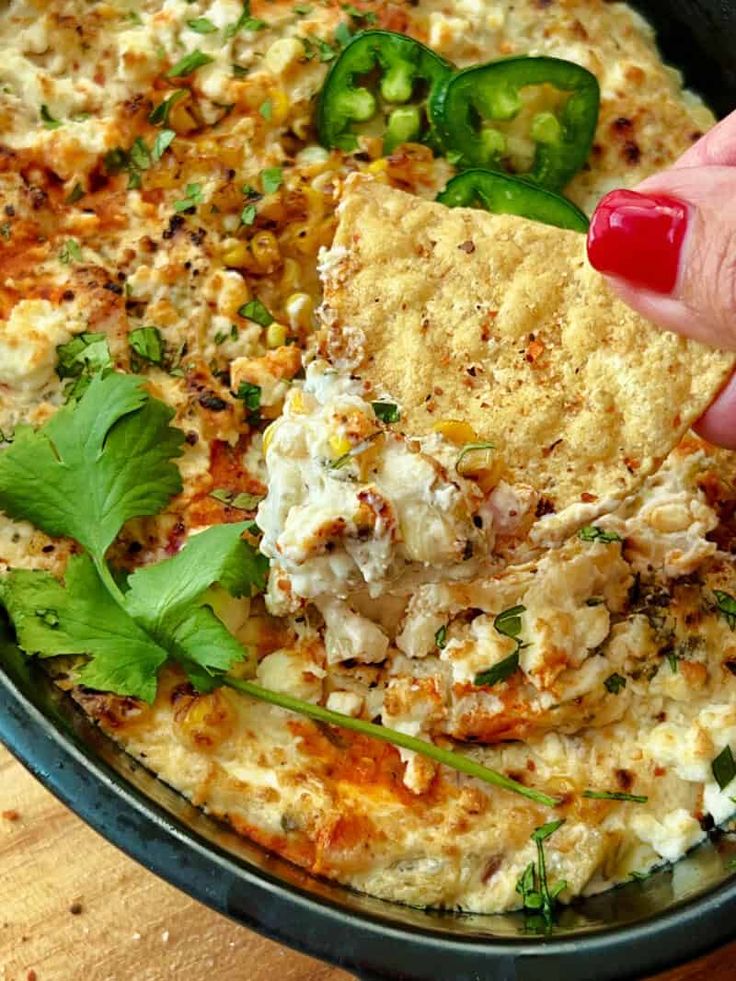 a person is dipping some food into a bowl with tortilla chips and cilantro