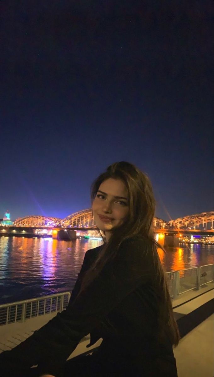 a woman standing on the side of a bridge next to a body of water at night