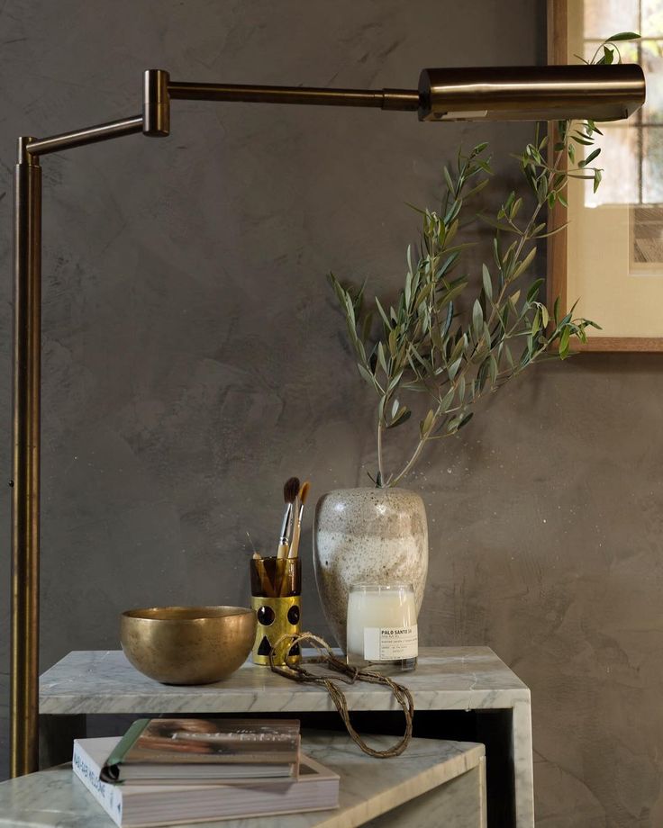 an olive tree in a glass vase on a marble side table next to a gold bowl