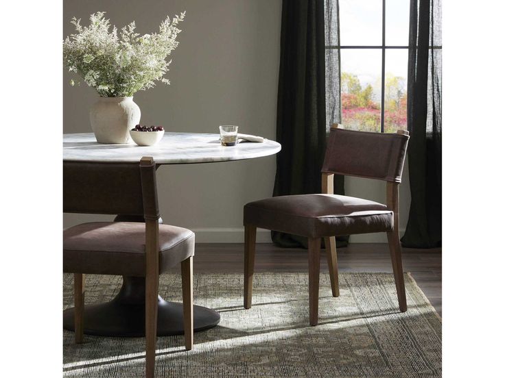 two chairs and a table in front of a window with flowers on the table next to it