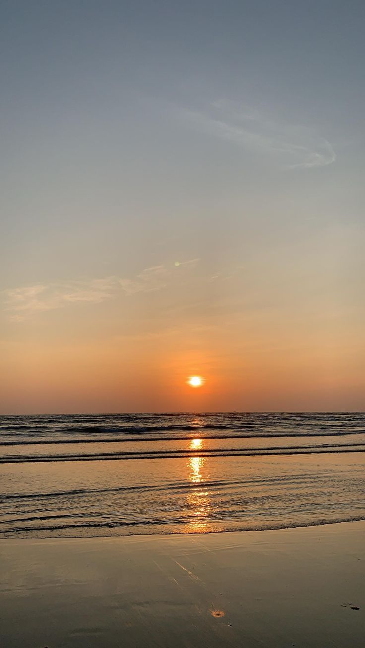 the sun is setting over the ocean with people walking on the beach