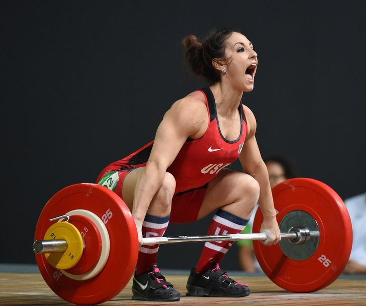 a woman is squatting on a barbell with her mouth open and hands in the air