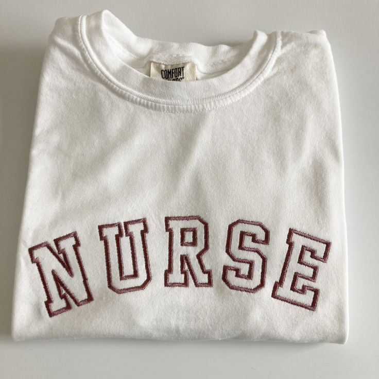 My absolute favorite tee! This 'NURSE' tee can be customized to your preferred thread color and is stitched on a Comfort Colors short sleeve unisex tee.  Please wash on gentle cycle and dry on low.  If you are wanting a different design, wording, or a different clothing style, please send me a message so we can discuss the details. Please include thread color at checkout If you need this order rushed, please add these to your cart: https://www.etsy.com/listing/1043569716/rush-my-order-for-t-shir White Relaxed Fit T-shirt With Letter Embroidery, Varsity Crew Neck Tops With Embroidered Graphics, College Crew Neck T-shirt With Letter Print, College T-shirt With Embroidered Graphics And Relaxed Fit, Graphic Tee With Embroidered Graphics For College, Crew Neck T-shirt With Letter Embroidery For College, Varsity Cotton T-shirt With Embroidered Graphics, College Crew Neck T-shirt With Embroidered Logo, Collegiate Crew Neck Top With Embroidered Graphics