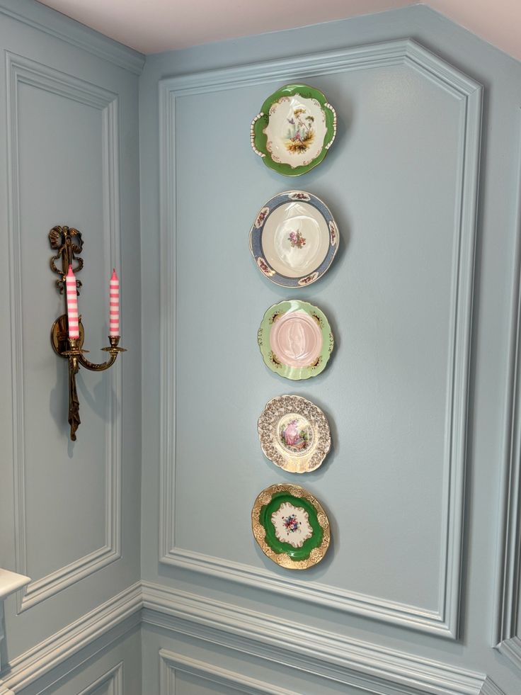 plates are arranged on the wall in this blue room with pink candlesticks and candle holders