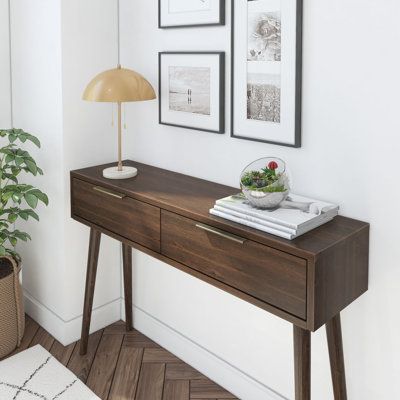 a wooden table with two pictures on the wall above it and a lamp next to it