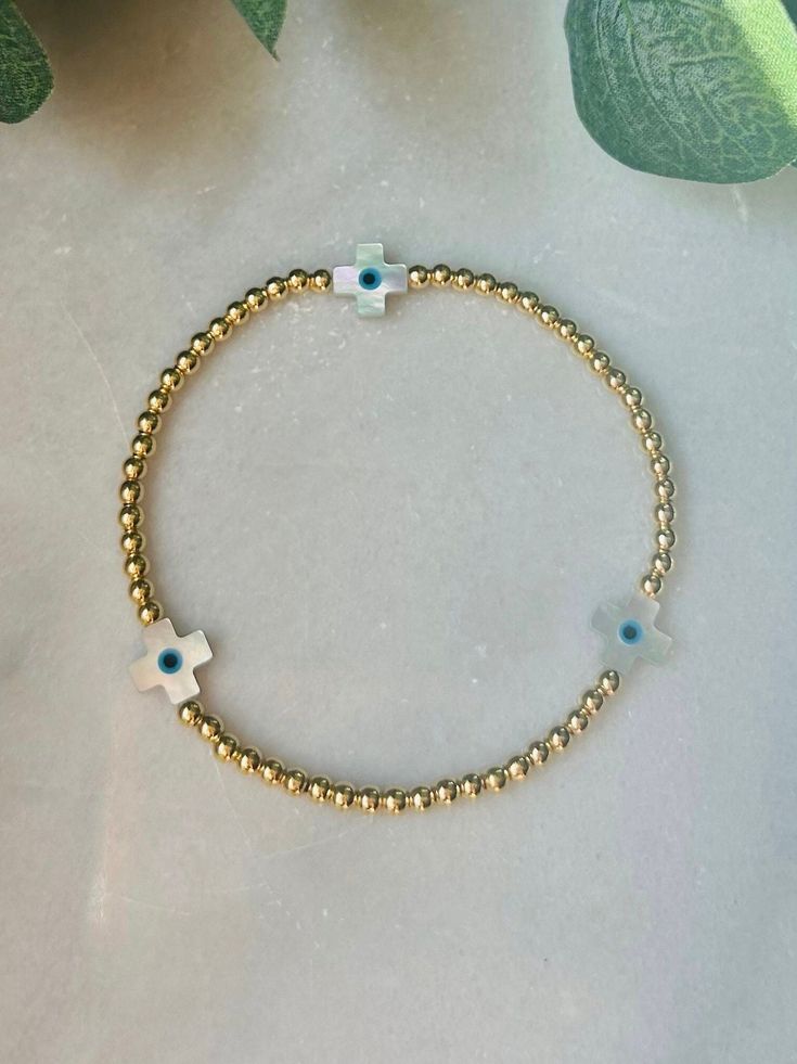 - Cute and dainty evil eye gold beaded bracelet with 18k gold filled beads and white shell cross beads. Excellent stacking addition to other gold beaded bracelets. Coordinating  anklet in shop. Bracelet is beaded on high quality stretch cord. - The evil eye is said to guard against misfortune and believed to protect the person who wears it from any ill-will. **evil eye on cross is very small. A true minimalist look** - 3mm 18k gold filled beads   10x8mm shell cross with evil eye    - Each purchase is sent in a velvet drawstring jewelry bag making the perfect gift for someone special or just for you. - To care for your bracelet, please roll on and off the wrist. Repeated stretching can wear the elastic over time. Avoid excessive contact with water and chemicals. Keep stored in jewelry bag. Gold Spiritual Beaded Cross Bracelets, Gold Beaded Cross Bracelets For Spiritual Style, Gold Cross Beaded Bracelets For Spiritual Style, Spiritual Gold Beaded Cross Bracelets, Gold Cross-shaped Spiritual Beaded Bracelets, Adjustable Gold Beaded Cross Bracelets, Handmade Gold Cross Bracelets, Handmade Gold Bracelet With Cross Shape, Gold Beaded Bracelets With Evil Eye