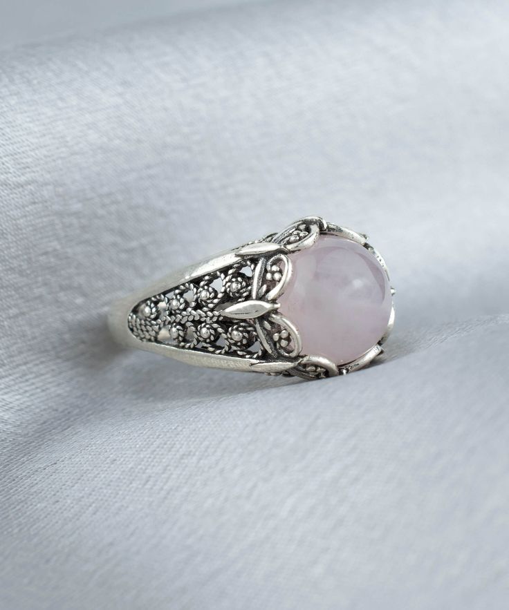 Elevate your style with this stunning Handmade Filigree Art Rose Quartz Gemstone Women Silver Cocktail Statement Ring. The 10mm cabochon round-cut Rose Quartz gemstone set in an elegant silver band measures 13.50mm in length and width, creating a beautiful contrast between the soft pink hues of the gemstone and the silver metal. Crafted with intricate details that showcase the beauty of filigree, an ancient art form originating from Mesopotamia and Anatolia, this exquisite ring is a true work of Elegant Adjustable Rose-colored Ring, Elegant Pink Cabochon Rings, Elegant Cabochon Ring With Round Stone, Elegant Sterling Silver Ring With Rose Design, Elegant Cabochon Rings, Elegant Jewelry With Round Stone Setting, Elegant Pink Oval Cabochon Ring, Classic Pink Cabochon Rings, Elegant Rings With Rose Design