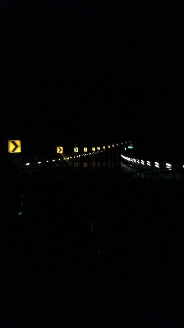 a train traveling over a bridge in the dark with traffic lights on it's sides