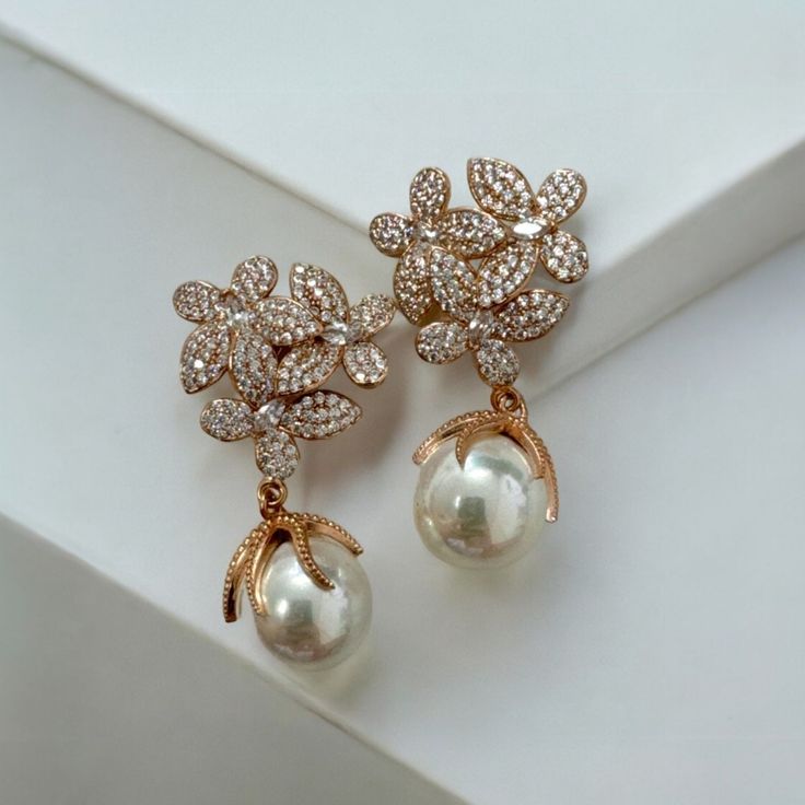 Make a stunning statement this season with the gorgeous Flowers Pearl Earrings. These elegant earrings feature an exquisite floral-inspired design for timeless sophistication. Three delicate blossoms set as if in a bouquet boast an abundance of dazzling cubic zirconia on each petal with a beautiful pearl dangling provocatively beneath, giving it an extra special touch of sophistication. Pearls are an elegant, classic choice that will never go out of style. This timeless gemstone will take you to every significant event of your life. Whether you're the stylish bride with a taste for timeless elegance, or just wanting to add a dash of sparkle to your everyday wardrobe, these earrings will be all you need. Handcrafted in 925 sterling silver dipped in 18ct rosegold. Pearls. Cubic zirconia.  Pa Formal Rose Gold Flower Earrings, Elegant Rose Gold Flower-shaped Pearl Earrings, Elegant Jewelry In Rose Gold With Flower Shape, Elegant Formal Jewelry With Rose Design, Rose Gold Flower Jewelry For Evening, Elegant Rose Gold Jewelry With Flower Shape, Elegant Rose Design Jewelry For Formal Occasions, Elegant Rose Gold Drop Bridal Earrings, Luxury Floral Bridal Earrings For Formal Events