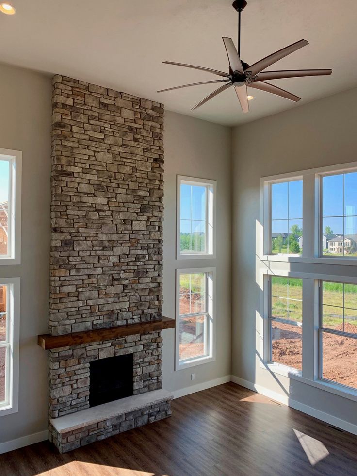 an empty living room with large windows and a brick fireplace in the middle of it