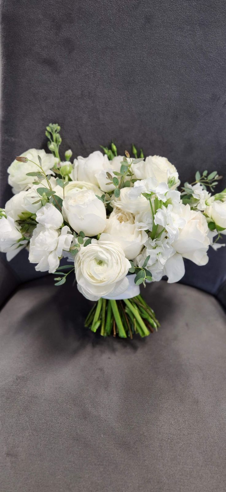 a bouquet of white flowers sitting on top of a gray chair next to a wall