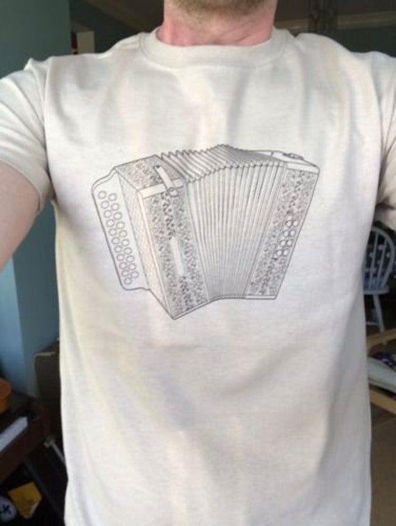 A stylish Melodeon (Hohner Pokerwork model design) T Shirt!  Unisex. Stand out from the crowd with this unique piece of quality clothing.  Available in 2 colours; Sand or Natural, on a quality Gildan Ultra-Cotton base shirt. Great for Folk Musicians, Morris Dancers, Melodeon players, Folk enthusiasts! Show off the classic, iconic design of this instrument! Condition:BRAND NEW Neckline:Crew Neck Sleeve Length:Short Sleeve Design:Graphic Size:S, M, L, XL Brand:Gildan Exact Material:Ultra Cotton Theme:Morris, folk, Music, Festival Material:Cotton Fit:Regular Colour:Sand or Natural Type:T-Shirt Size Type:Regular Unisex Music-themed Tops With Screen Print, Unisex Music-themed Screen Print Top, Music-themed Unisex Screen Print Top, Morris Dancers, Morris Dancing, Folk Musician, Music T Shirt, Acoustic Music, Music Tees