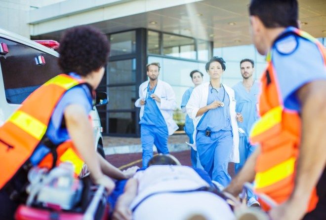 several medical personnel walking towards an ambulance with a man on the ground in front of them