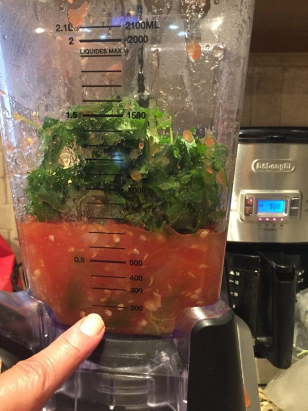 a blender filled with lots of vegetables in it's side dish and being held up by a hand