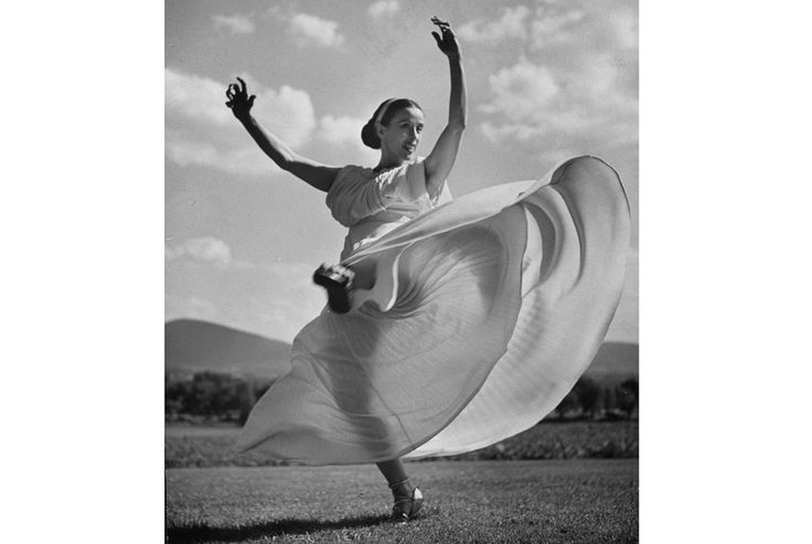 a woman in a long dress is dancing on the grass with her arms spread out