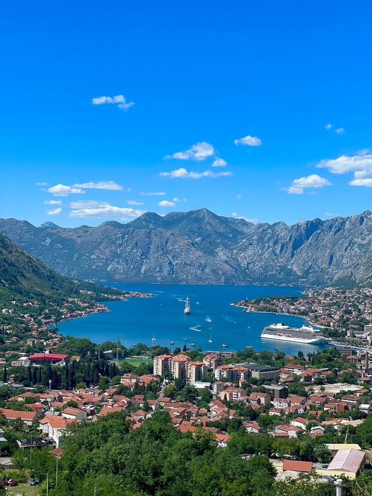 an aerial view of a town and the ocean with mountains in the background, surrounded by greenery