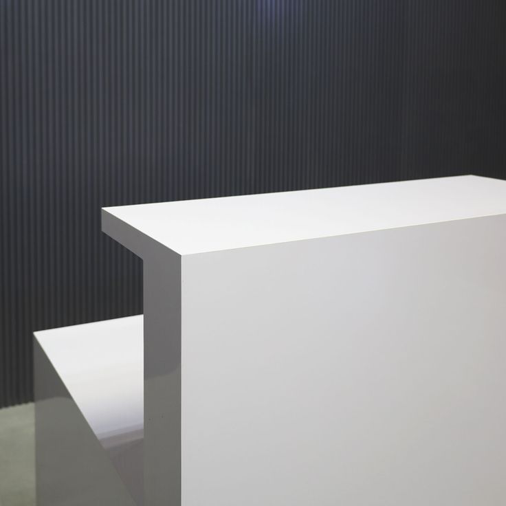 a white counter sitting in front of a black wall with vertical stripes on it's side