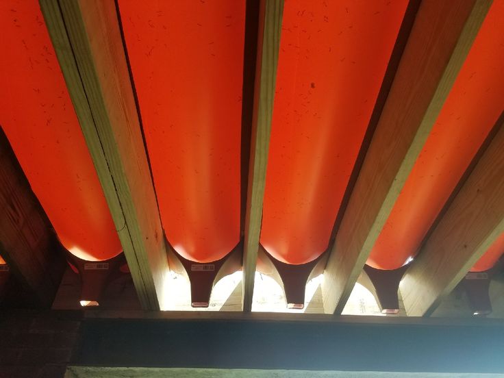 the underside of a wooden structure with bright orange plastic tubes on it's sides