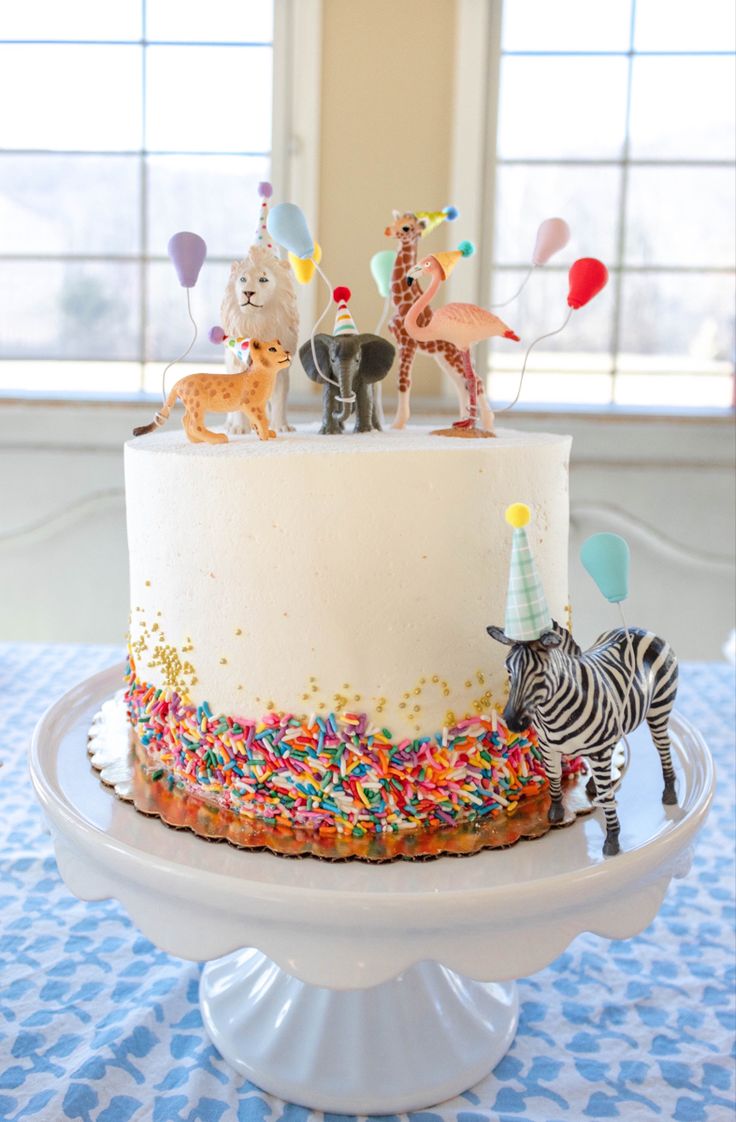 a birthday cake decorated with animals and balloons on a table in front of a window