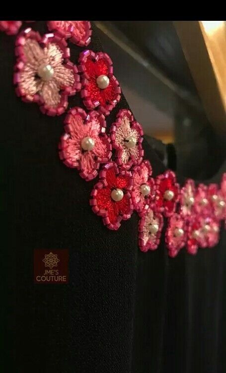 a dress with pink flowers and pearls on the collar is hanging in front of a mirror