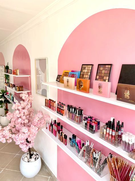 a pink and white room with shelves full of cosmetics, perfumes and flowers in vases