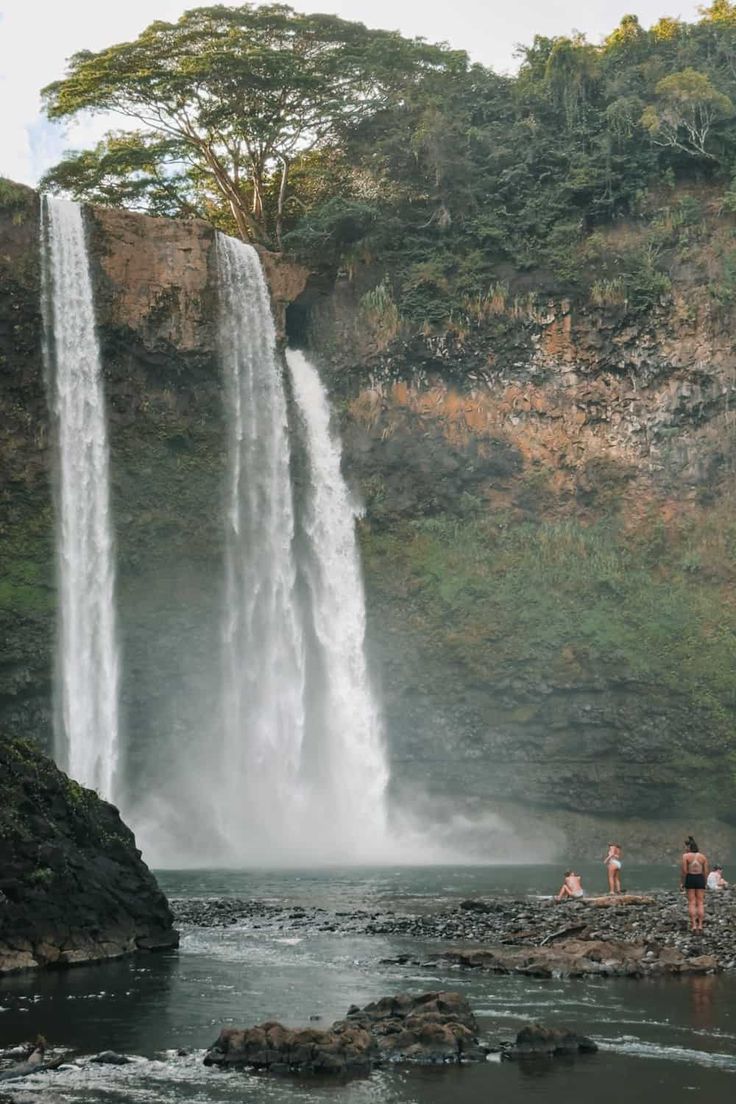 two people standing at the base of a waterfall