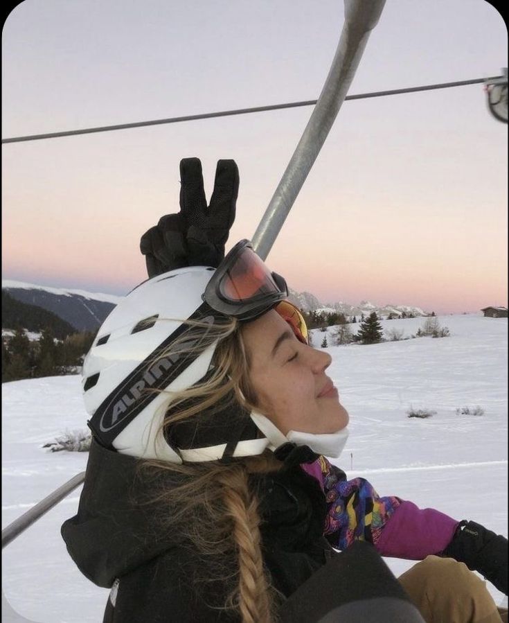 a woman riding on the back of a snow covered ski lift holding onto her skis