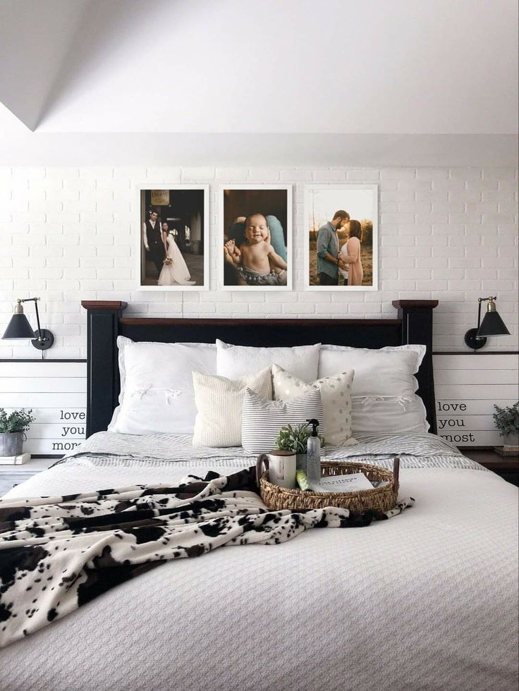 a white bed with black and white decor on the headboard, two pictures above it