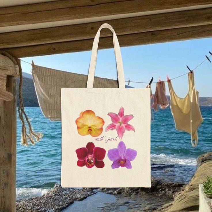 a bag hanging on a clothes line by the ocean with flowers painted on it,